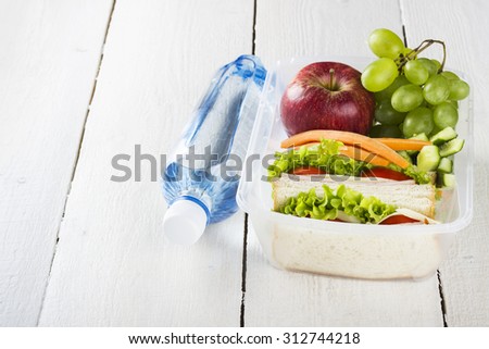 Lunchbox with a sandwich, vegetables, fruit and water bottle on a white wooden background