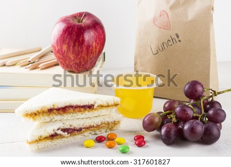 Lunchbox in school: sandwich with peanut butter and jam, apple, grapes, jelly on a white wooden background