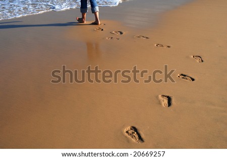 A Female walking on the beach, with a string of footprints behind