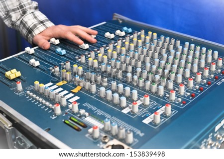 sound engineer's hand moving sliders on audio mixing board