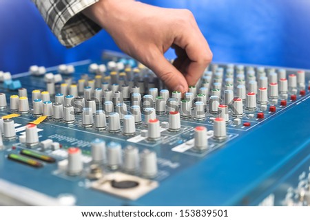 sound engineer\'s hand moving sliders on audio mixing board