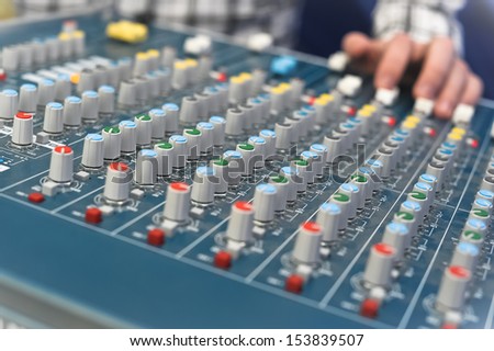 sound engineer\'s hand moving sliders on audio mixing board