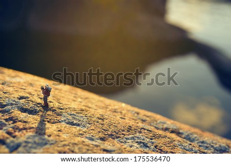 Male hiker catching breath while climbing, sky reflecting in water below, miniature figure