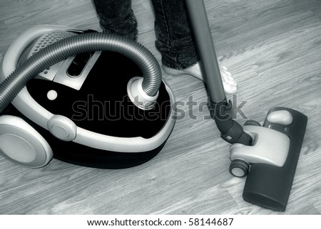 Barefoot female vacuum-cleaning, close-up in black and white