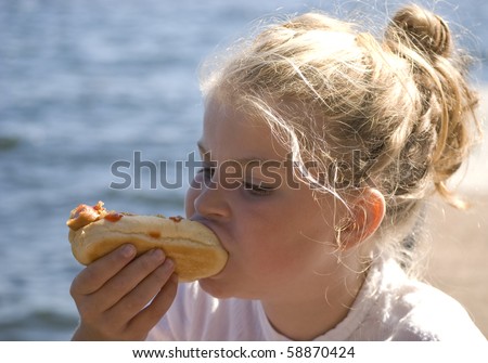 Girl eating hot dog at the beach a sunny summer day