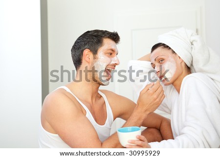 Loving pair couple making cosmetics at home. girlfriend applies beauty mask to husband in living room