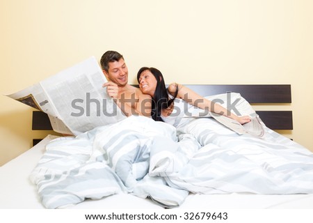 Smiling funny couple man and woman in bed reading newspaper on their vacations