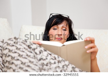 Confident indoor reading woman relaxing on couch while learning from book lecture for successful life