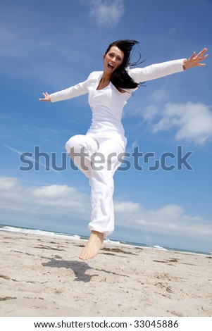 Happy holiday jumping woman on the beach with outstretched arms and smiling positive expression