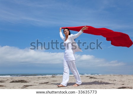 Woman walking on the windy coast with red tissue in white clothes feeling free on empty beach and celebrating her vacations