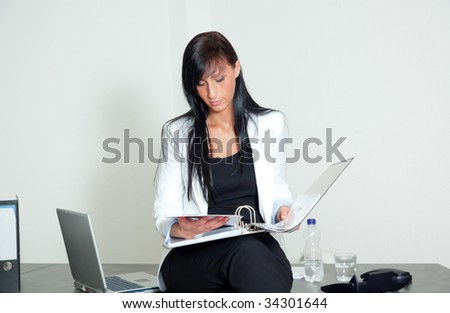 Woman sitting on desk holding ring binder while looking at sales numbers for success business