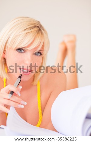 Learning blond student girl making college university homework at home holding pen and lying down on couch