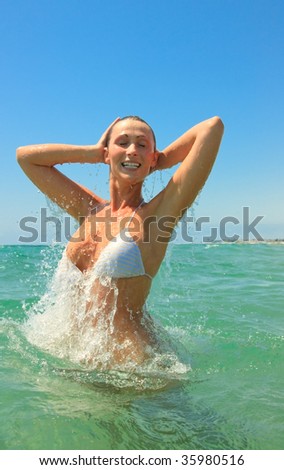 Colorful jumping splashing girl with a lot of waterdrops standing in the sea coast ocean on the beach feeling free