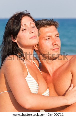 Natural suntanning loving couple of a young relationship embracing holding arm around beyond blue sea