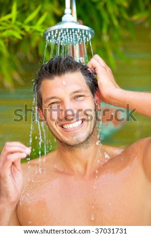 Attractive man under floating water in nature showering while water spray and splash down his beauty face