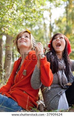Two playing girls in forest park throwing leaves and foliages in warm winter clothes on beautiful weather day