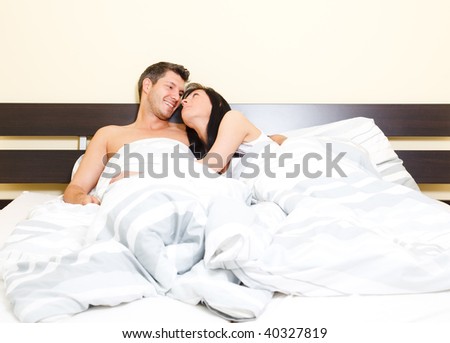 Scenic in bedroom of pair of loving young couple lying in bed looking eachother romantic while cuddling and embracing