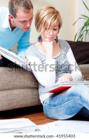 Scenic young family couple at home indoors in living room doing paperwork sitting on couch and floor with lot of paper documents