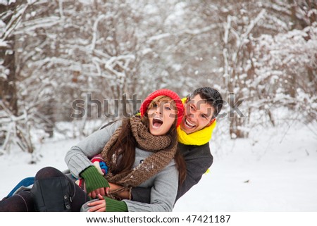 Playful winter couple sledding on sled in park