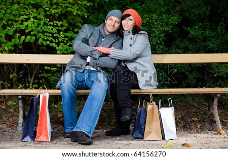 Pair of man and woman couple sitting on bank in park garden after shopping with bags