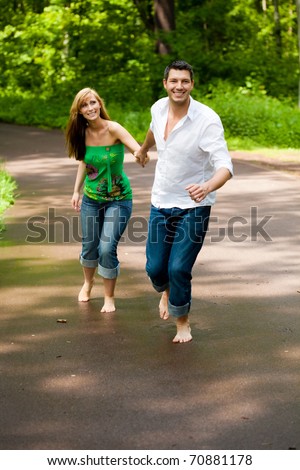 Happy running barefoot couple of two with trees in background smiling walk