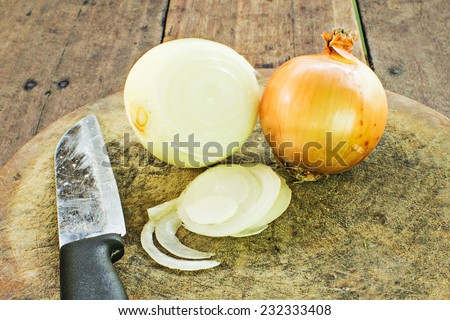 Onion with a knife in the corner of a butcher block.