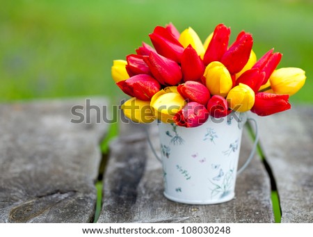 red and yellow tulips in a bucket on garden table