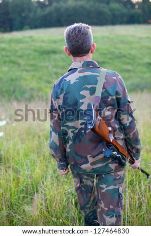 Male hunter in camouflage clothes walking on the field