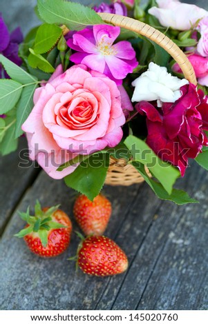 basket with roses and strawberries on garden table on a beautiful summer day
