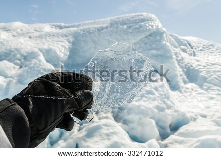 Hand with glove holding a transparent ice piece with snow and ice background