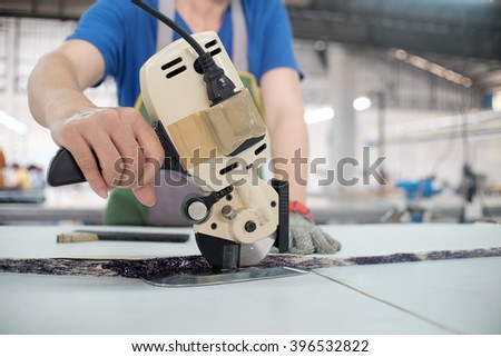 Female worker on a sewing manufacture uses electric cutting fabric machine. Sewing production line.