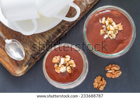 Layered cream jelly with chocolate sauce and walnuts, served in a jar on stone background, top view