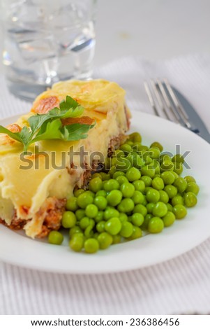 Shepherds pie, served with green peas and water on white background, closeup