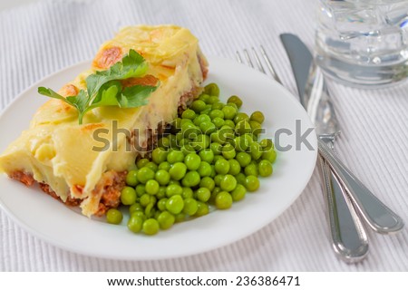 Shepherds pie, served with green peas and water on white background