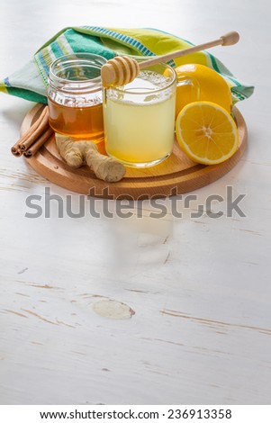 Cold care - tea, honey, lemon, ginger, cinnamon sticks on white wood background