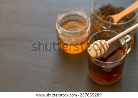 Black tea with honey and dry black tea in glass jar on dark stone background