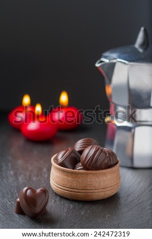 Chocolate candies in wood bowl, candles, coffee maker, on dark stone background