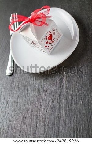 Present, white lacy box with red chocolate candies on white plate dark stone background