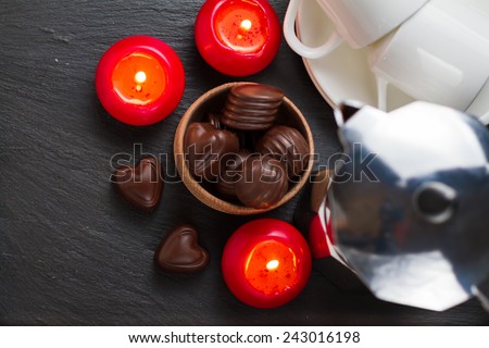 Chocolate candies in wood bowl, candles, coffee maker and cups on dark stone background