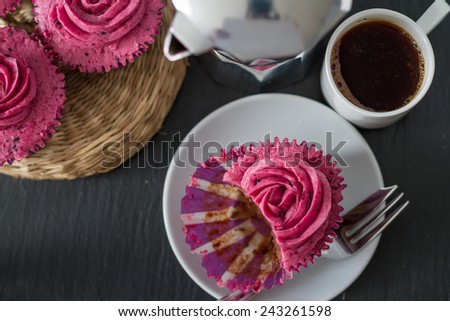 Chocolate and blackcurrant buttercream cupcake, bite, coffee and coffee maker on dark stone background