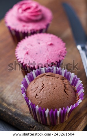 Cupcake decoration - chocolate and blackcurrant buttercream cupcakes on different stages, knife on wood background