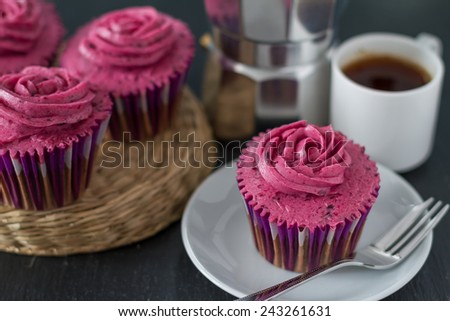 Chocolate and blackcurrant buttercream cupcake, coffee and coffee maker on dark stone background