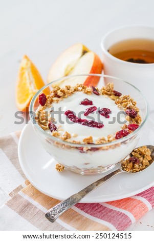 Smile face - apple granola with yogurt and jam in glass bowl, oranges, tea, white wood background