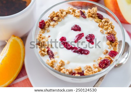 Smile face - apple granola with yogurt and jam in glass bowl, oranges, tea, white wood background, top view, closeup