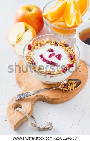 Smile face - apple granola with yogurt and jam in glass bowl on apple shaped wood board, oranges, tea, white wood background