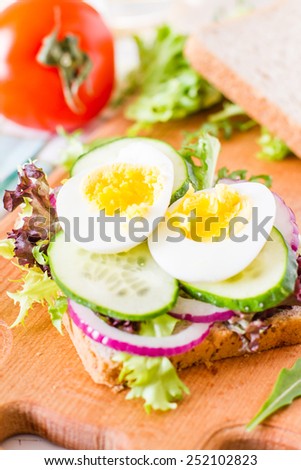 Egg sandwich, tomato and salad on wood board, white wood background, closeup