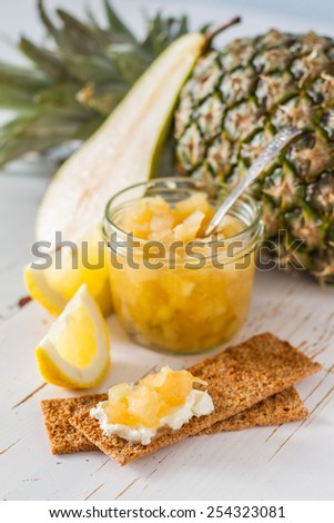 Pineapple jam in glass jar, pineapple and lemon slices, crisp bread, white wood background