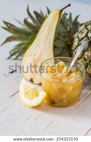 Pineapple jam in glass jar, pineapple and lemon slices, white wood background