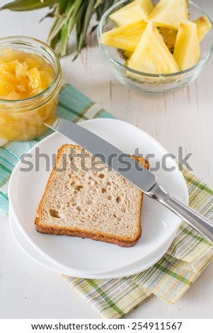 Breakfast - toast, pineapple jam, pineapple slices, tea, plaid napkin, white wood background, top view