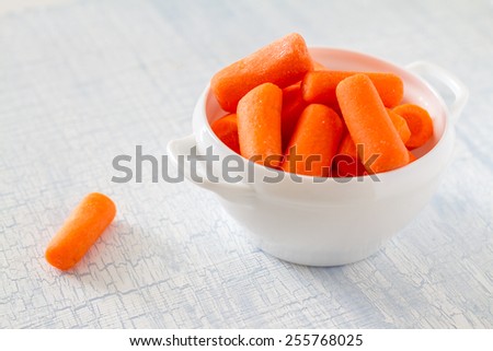 Baby carrot sticks in white bowl on light blue wood background